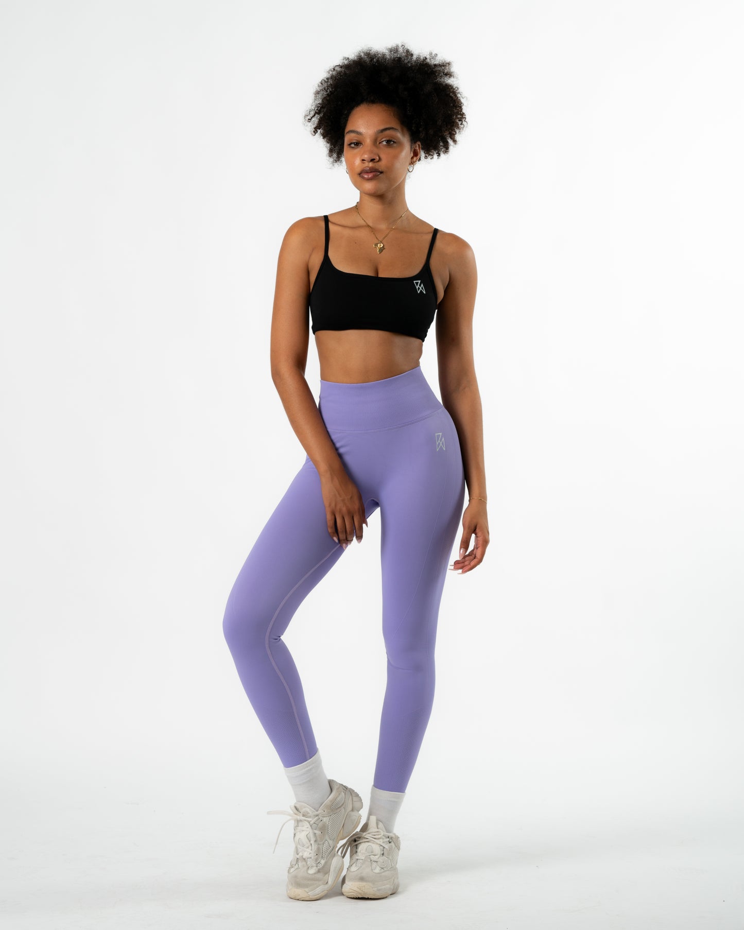 Woman wearing a black sports bra and purple leggings on a white background